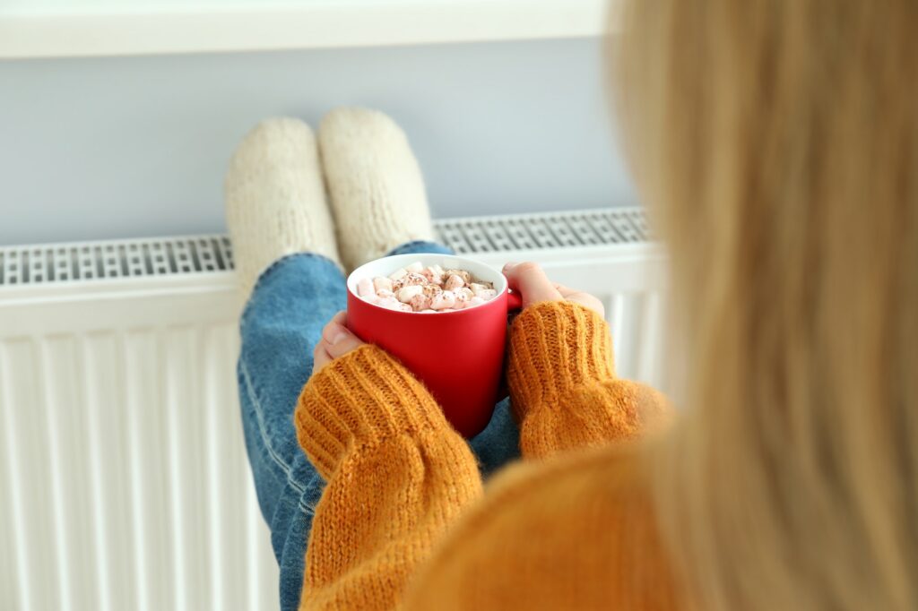 Concept of heating season with girl sitting near radiator